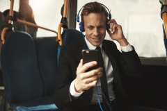 Smiling businessman reading messages and wearing headphones on a bus